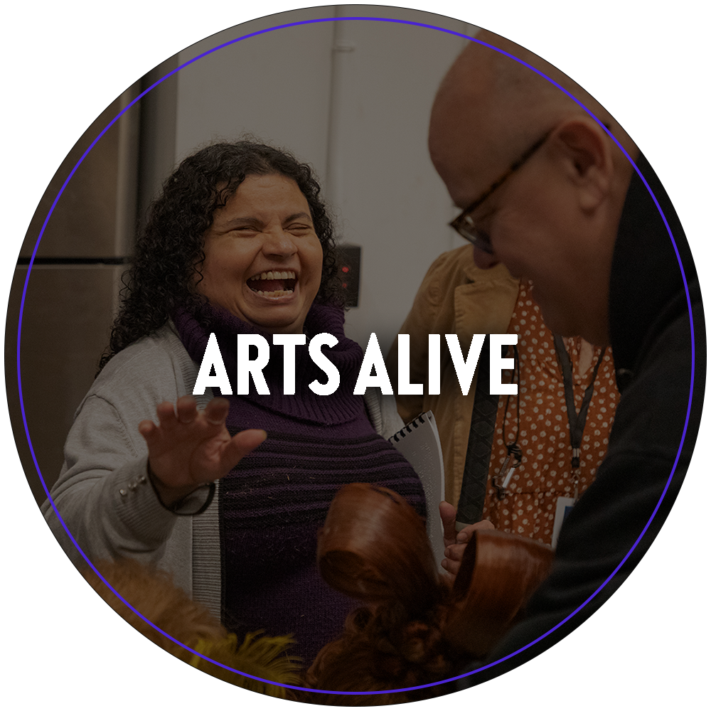 A circular image of a vision impaired woman with a large smile. She is being presented a costume piece to touch as part of Broadway Sacramento's Arts Alive tactile experience program, where guests can interact with props, costumes and production crew. Text in the center of the image reads "Arts Alive". 

You can click the image to redirect to the Arts Alive web page. 